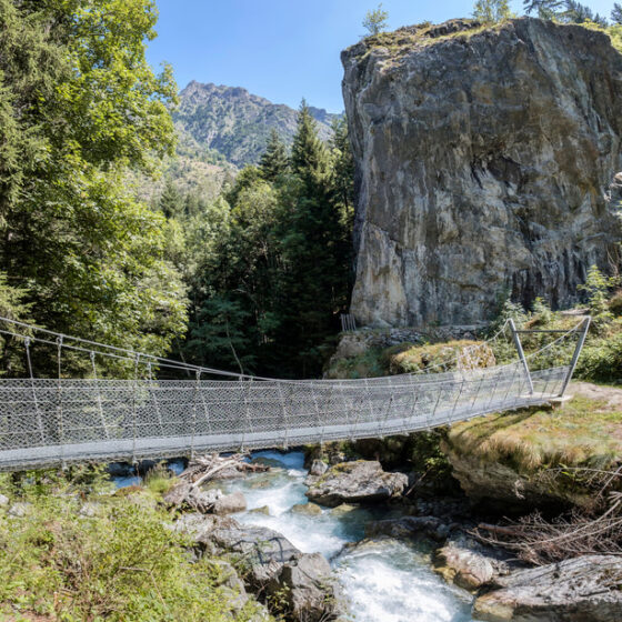 Passerelle suspendue franchissant le torrent au pied d'une falaise